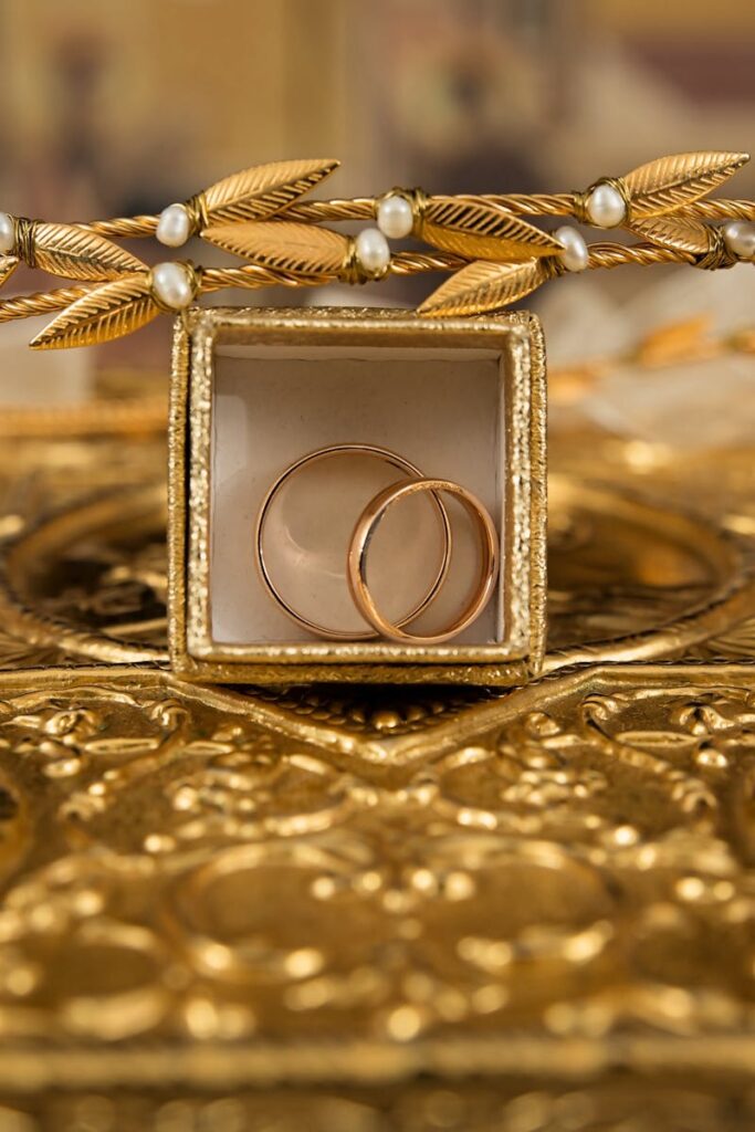 Close-up of gold wedding rings and a delicate tiara on an ornate golden background, symbolizing luxury and elegance.